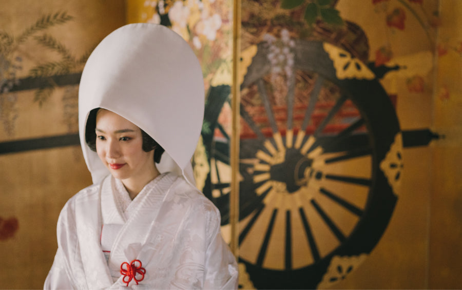 Bride in white shiromuku kimono and wataboshi hood in front of a gold folding screen at a Shinto wedding