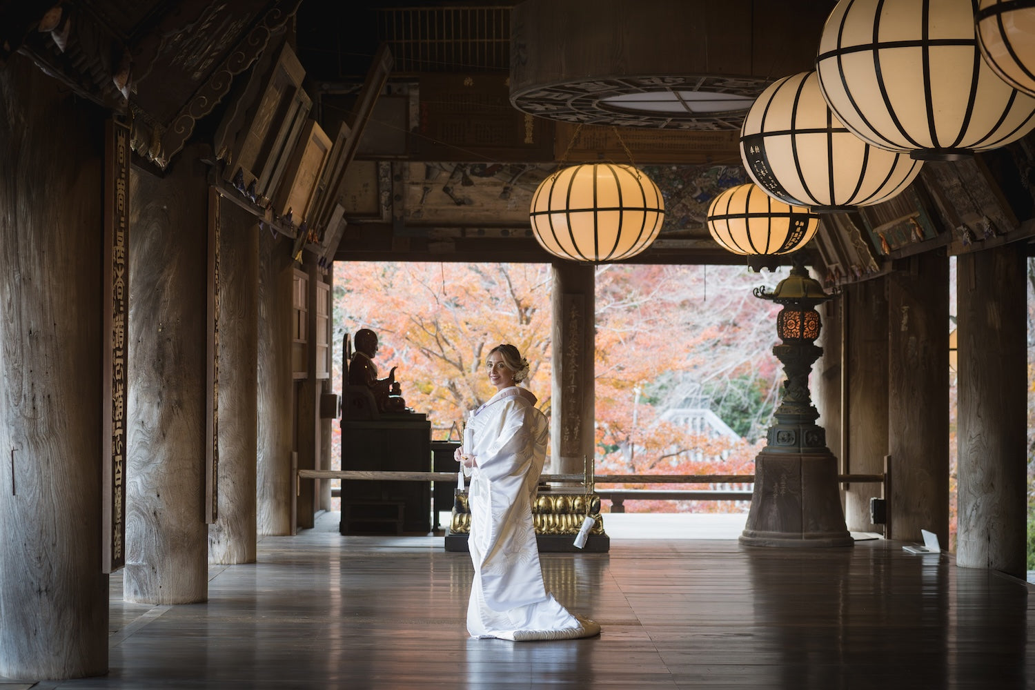 Bride walking a temple corridor overlooking autumn foliage after the ceremony
